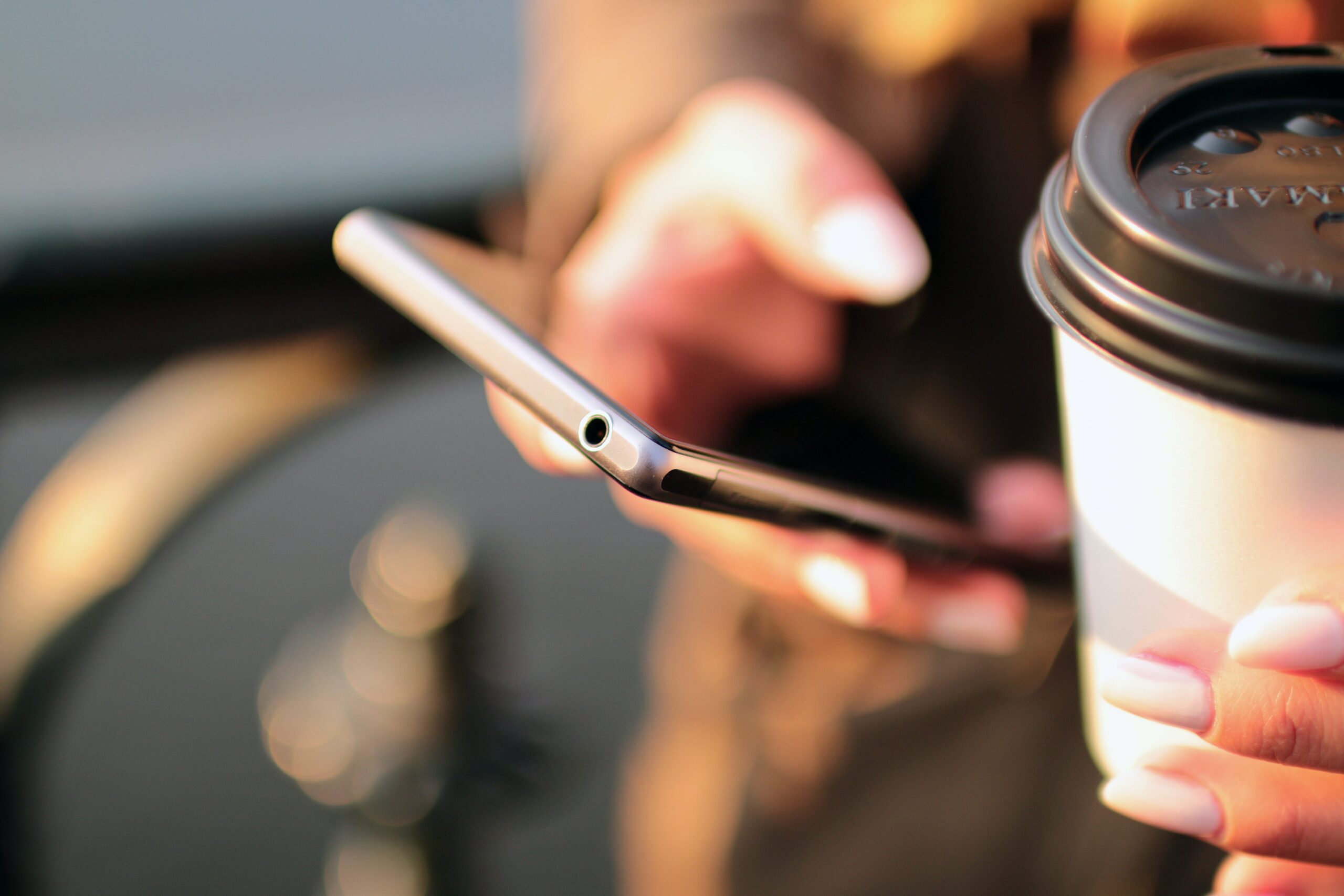 Iemand met een wegwerp koffiecup en telefoon in de handen